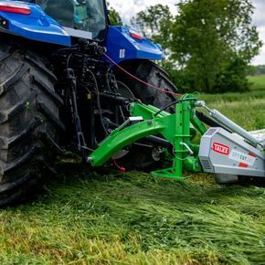 Zielona kosiarka dyskowa OPTI CUT 280 firmy TALEX kosi trawę z niebieskim ciągnikiem