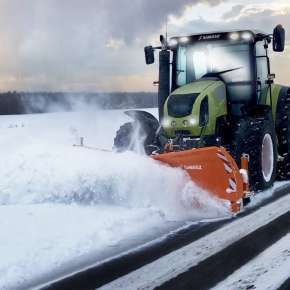 Zielony ciągnik rolniczy z podczepionym pomarańczowym pługiem do śniegu PSV 301 firmy Samasz odśnieża pobocze drogi www.korbanek.pl