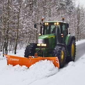 Pomarańczowy spychacz do śniegu PSV firmy Samasz podczepiony do zielonego traktora rolniczego odśnieża polną drogę w lesie www.korbanek.pl