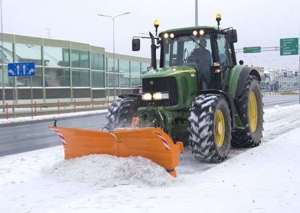 Pług do śniegu PSV firmy Samasz. Pomarańczowy spychacz zawieszony na ciągniku John Deere odśnieża ulicę