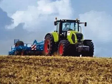 Traktor Claas Axion 840 jadący po polu z zaczepioną maszyną towarzyszącą Ciągnik Claas Axion 840 z tylnym TUZ o udźwigu 9676 kg