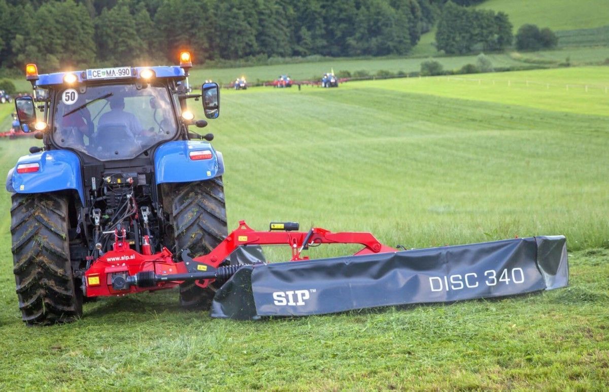 Czerwona kosiarka SIP typ SILVERCUT DISC 340S zaczepiona do niebieskiego ciągnika kosi łąkę www.korbanek.pl