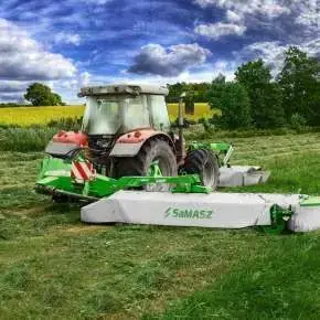 Widok z tyłu zielonej kosiarki dyskowej XT 390 firmy Samasz zawieszonej na czerwonym ciągniku podczas koszenia łąki www.korbanek.pl