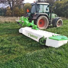 Widok z boku ciągnika rolniczego Fendt z podczepioną kosiarką dyskową Samasz typ XT 390 podczas koszeni użytków zielonych