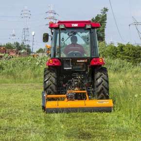 Pomarańczowa kosiarka mulczująca PIKO 130 firmy Samasz podczepiona do czerwonego traktora mulczuje nieużytek www.korbanek.pl