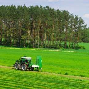 Zielony traktor jedzie po łące ze złożoną kosiarka bębnową Z010/2H firmy Samasz www.korbanek.pl
