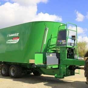 Zielony wóz paszowy dwuślimakowy DUO HD na osi Tandem firmy Samasz podczepiony do czerwonego ciągnika czeka na załadunek kiszonki www.korbanek.pl