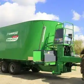 Zielony wóz paszowy dwuślimakowy DUO HD na osi Tandem firmy Samasz podczepiony do czerwonego ciągnika czeka na załadunek kiszonki www.korbanek.pl