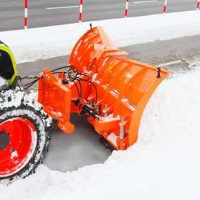 Widok z boku zielonego traktora rolniczego z zamontowanym pługiem do odśnieżania OLIMP firmy Samasz odśnieżającego ulicę www.korbanek.pl