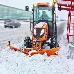 Pomarańczowy traktor rolniczy wraz z pomarańczowym spychem do śniegu CITY 180 firmy Samasz podczas odśnieżania zatoczkę przy przystanku www.korbanek.pl