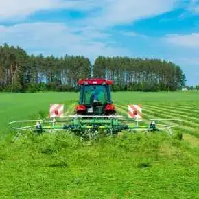 Czerwony traktor rolniczy przetrząsa skoszoną trawę za pomocą przetrząsacza zawieszanego P4-471 firmy Samasz www.korbanek.pl