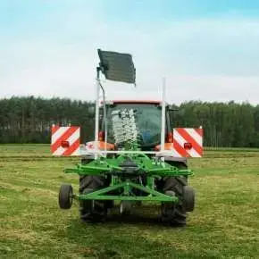 Zielona zgrabiarka zawieszona i złożona do pozycji transportowej na czerwonym ciągniku www.korbanek.pl