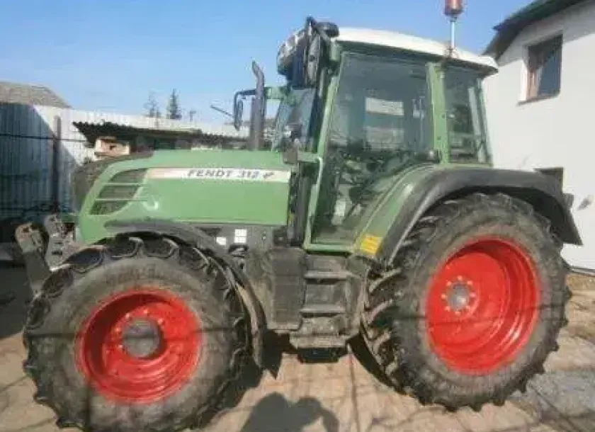 Zadbany używany ciągnik rolniczy Fendt 312 Vario widok na lewy bok pojazdu na tle zabudowań gospodarstwa 