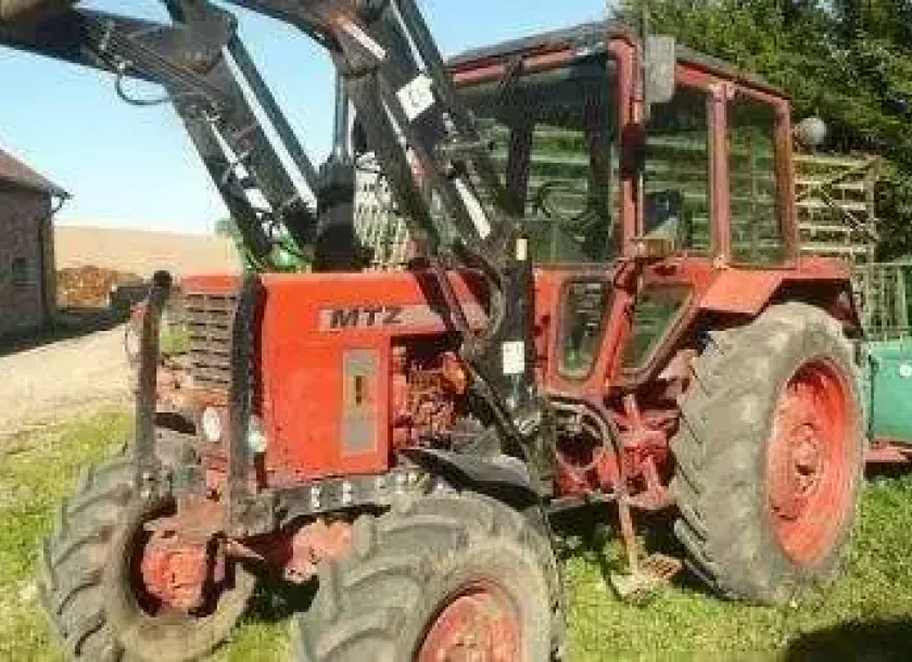 Czerwony używany ciagnik MTZ 82 z uniesionym wysoko ładowaczem Aromasz 