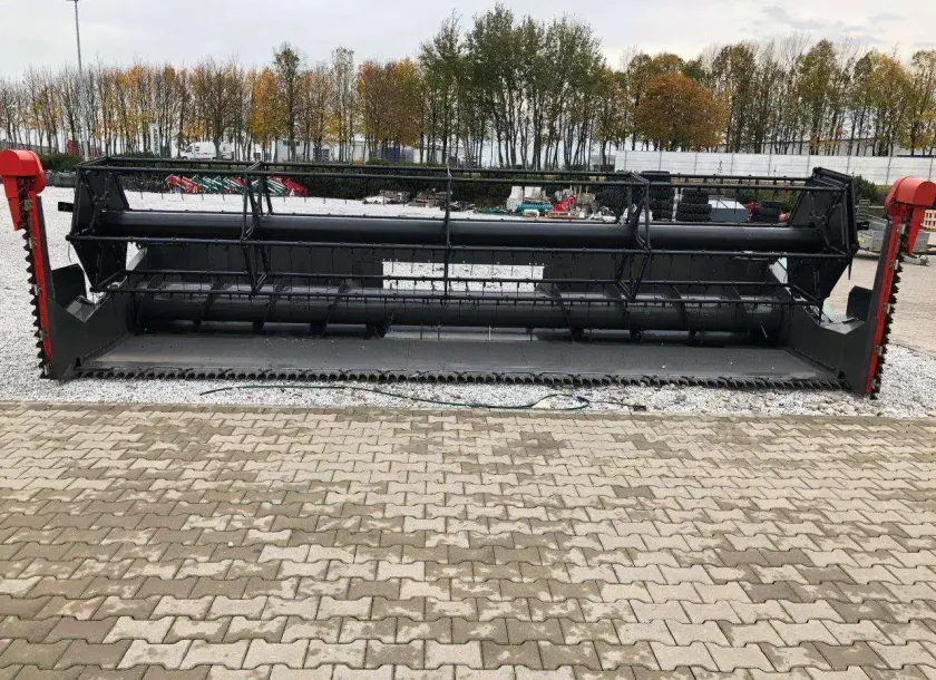 Heder do uzywanego kombajnu Fendt 6335 C na utwardzonym placu w tle wysokie drzewa