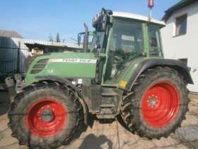 Zadbany używany ciągnik rolniczy Fendt 312 Vario widok na lewy bok pojazdu na tle zabudowań gospodarstwa 
