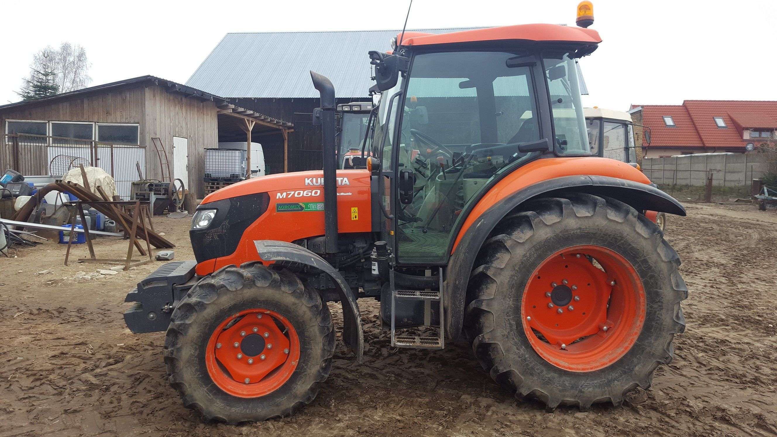 Lewy bok ciągnika m7060 marki kubota na tle gospodarstwa rolnego