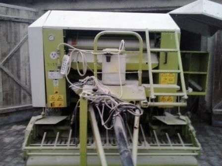 Używany Prasa Claas Rollant 255 RC  na tle otwartych drewnianych drzwi widok na dyszel 