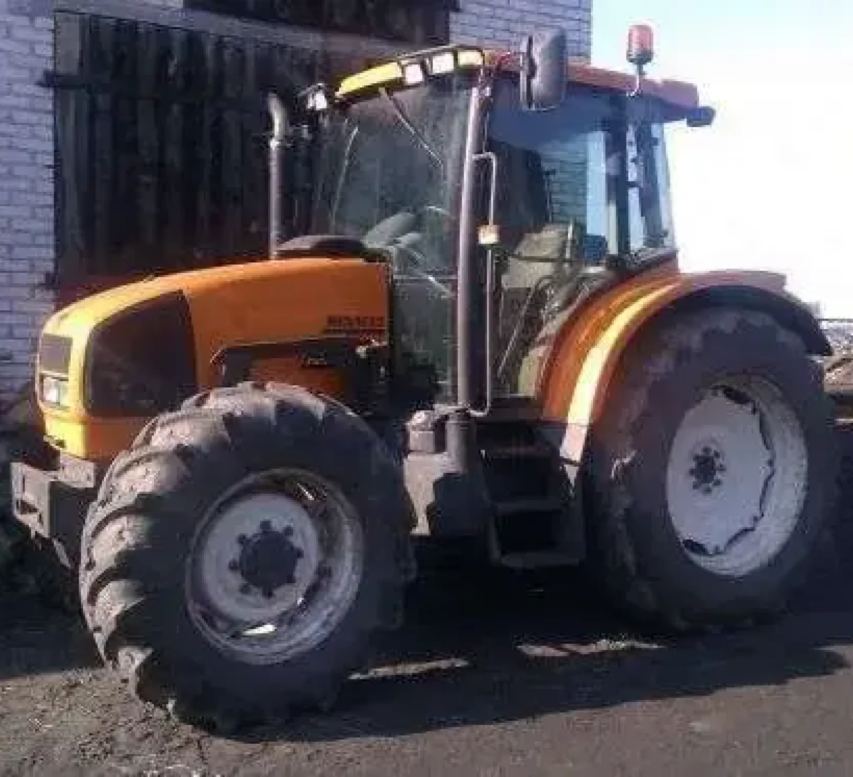 Używany żółty traktor rolniczy Renault Ares 550 RX w zabudowaniach gospodarstwa 