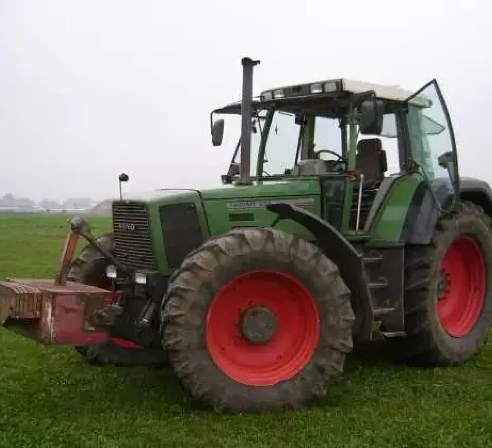 Używany ciągnik rolnicz Fendt 924 rocznik 1996 zaprezantowany na zielonym tle pola z czerwonym obciążnikiem przednim 