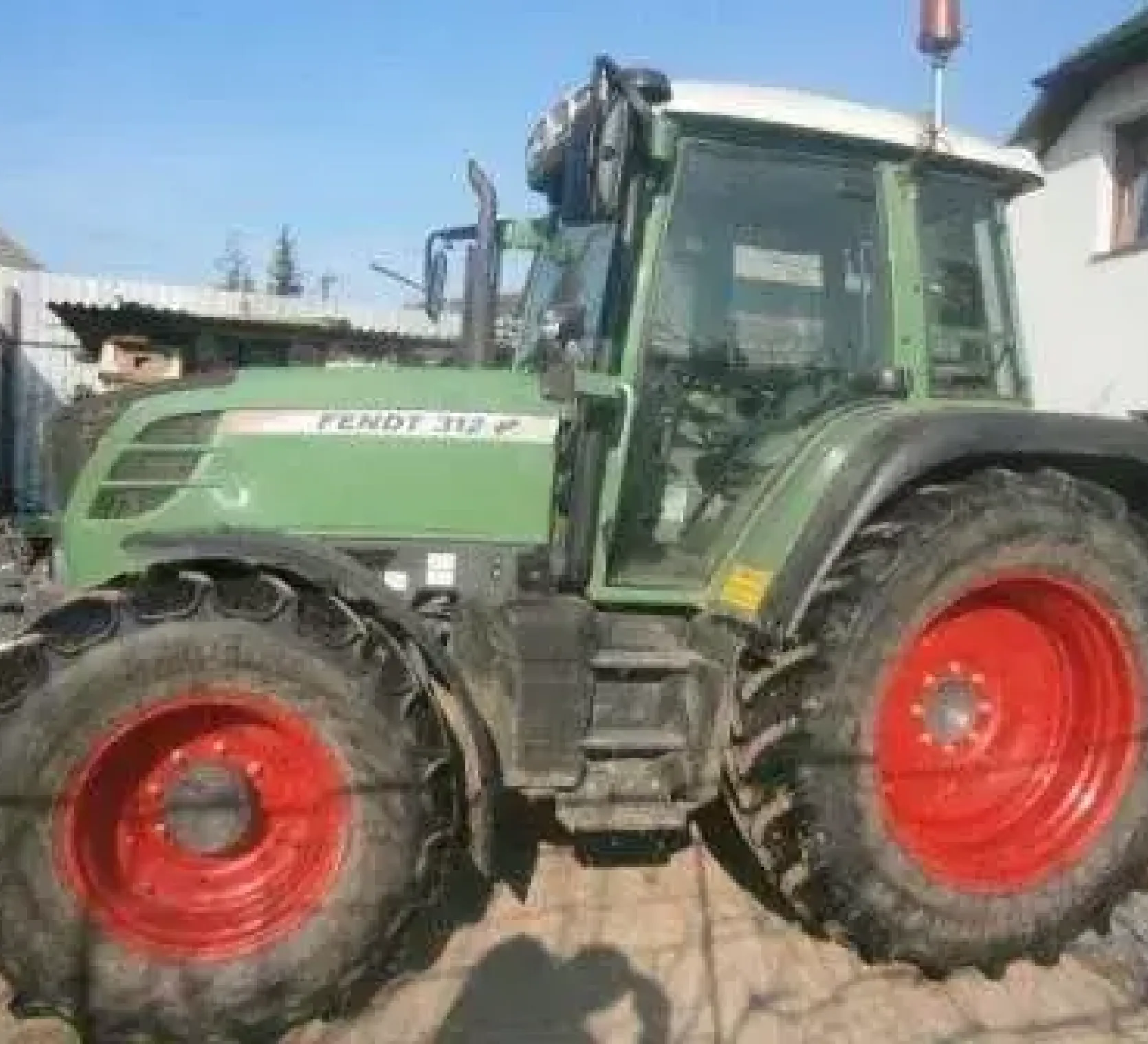 Zadbany używany ciągnik rolniczy Fendt 312 Vario widok na lewy bok pojazdu na tle zabudowań gospodarstwa 