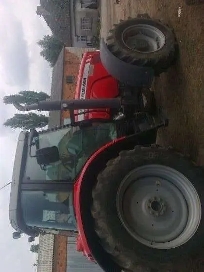 Ujęcie z boku na ciągnik rolniczy marki Massey Ferguson 5465 na tle gospodarstwa, kabina, koła, korbanek.pl