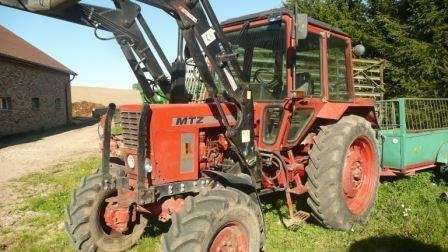Czerwony używany ciagnik MTZ 82 z uniesionym wysoko ładowaczem Aromasz 