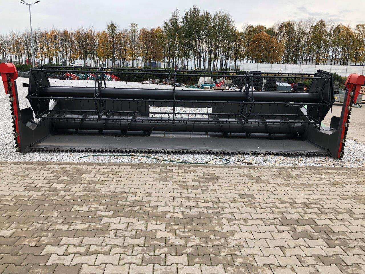 Heder do uzywanego kombajnu Fendt 6335 C na utwardzonym placu w tle wysokie drzewa