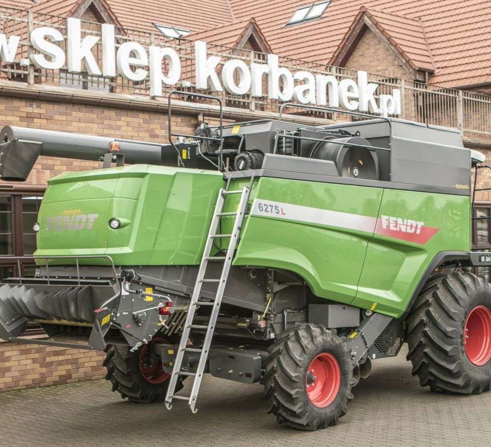 Prawy bok używanego kombajnu Fendt 6275 L  na tle sklepu części zamiennych społki Korbanek 