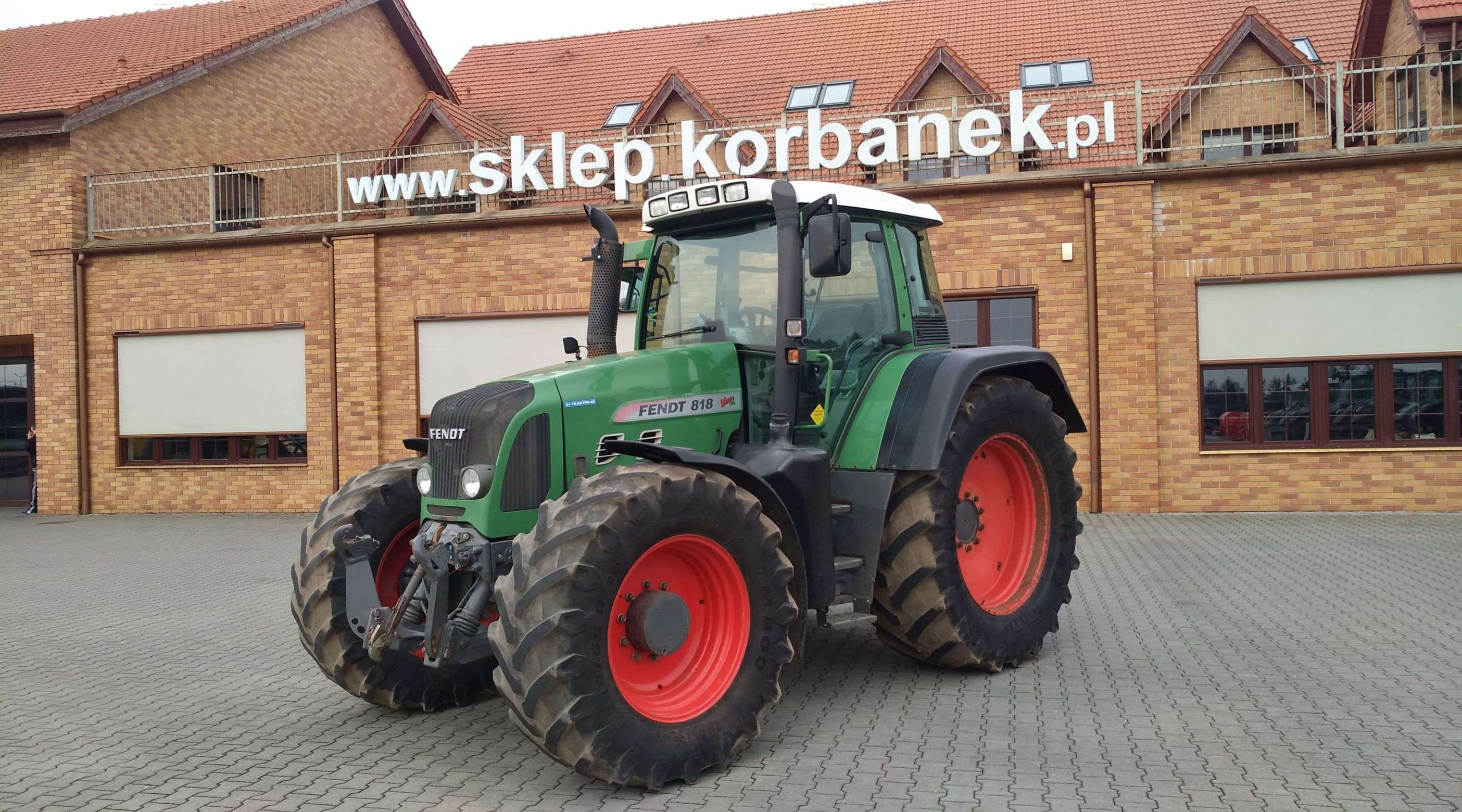 Ciągnik Fendt 818 Vario TMS na tle magazynu części Korbanek widok z lewej strony
