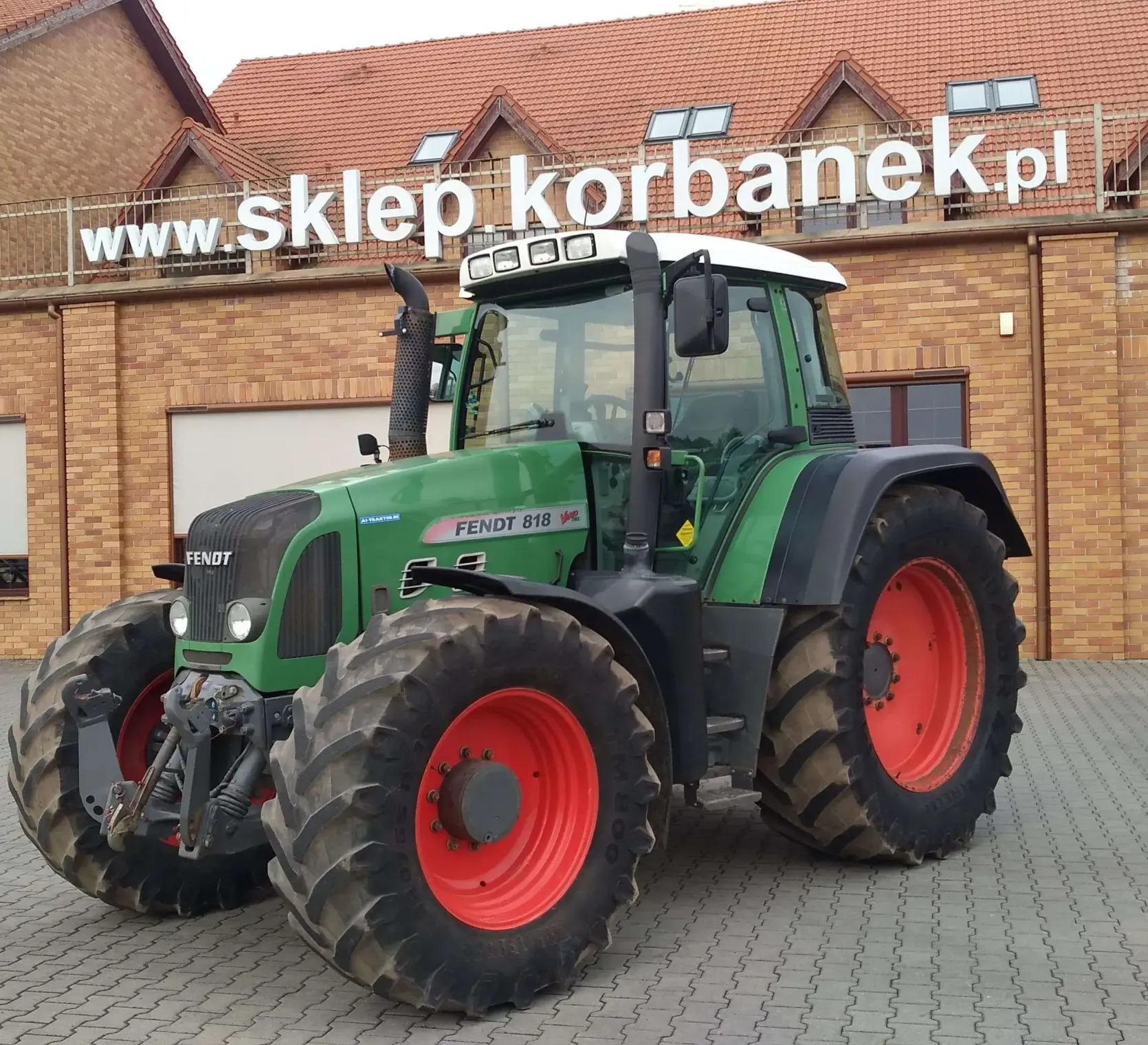 Ciągnik Fendt 818 Vario TMS na tle magazynu części Korbanek widok z lewej strony