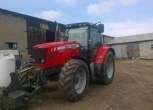 Widok na przód i bok ciągnika marki Massey Ferguson model 5465 czerwony traktor stoi na tle budynku gospodarczego