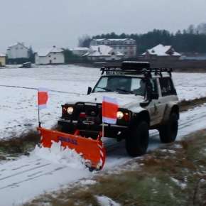 Pomarańczowy pług do śniegu SMART 220 zamontowany na białym terenowym samochodzie odśnieża polną drogę www.korbanek.pl