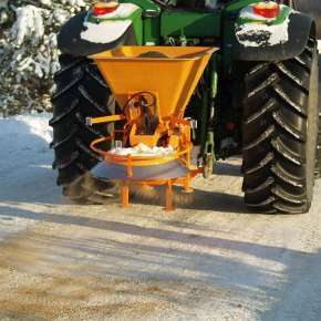 Pomarańczowa piaskarka SAND 400 firmy Samasz zawieszona na zielonym traktorze rolniczym posypuje pisakiem chodnik www.korbanek.pl