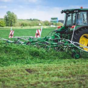 Traktor rolniczy w kolorze zielonym marki John Deere przetrząsa trawę przetrząsaczem zawieszanym P6-771 firmy Samasz www.korbanek.pl