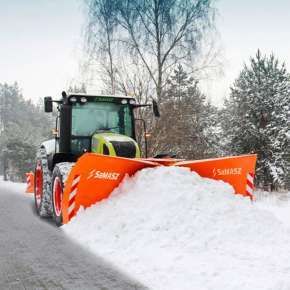 Widok od przodu zielonego ciągnika rolniczego, który przepycha zaspę śniegu za pomocą ciężkiego spychacza OLIMP firmy Samasz www.korbanek.pl