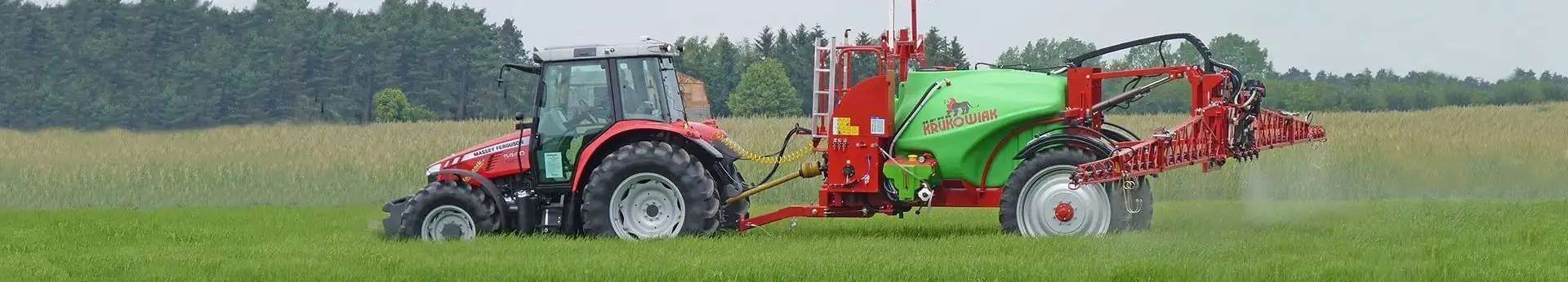 Ciągnik Massey Ferguson z opryskiwaczem Krukowiak przyczepianym Goliat Plus Czerwony Ciągnik Massey Ferguson pracujący w polu z opryskiwaczem przyczepianym Krukowiak Goliat Plus widok z boku podczas wykonywania oprysku